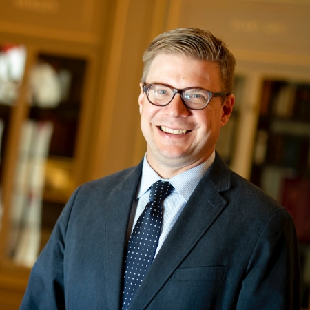 Thomas Hyry wears a dark blazer and purple tie and smiles at the camera